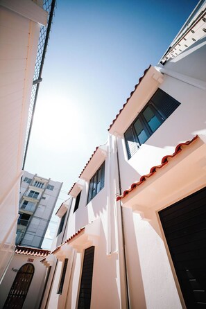Una calle estrecha con edificios blancos, un cartel de salida visible y un cielo despejado.