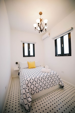 A bedroom with a bed, two windows, a chandelier, and an air conditioning unit.