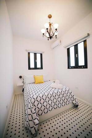 A bedroom with a bed, two windows, a chandelier, and an air conditioning unit.