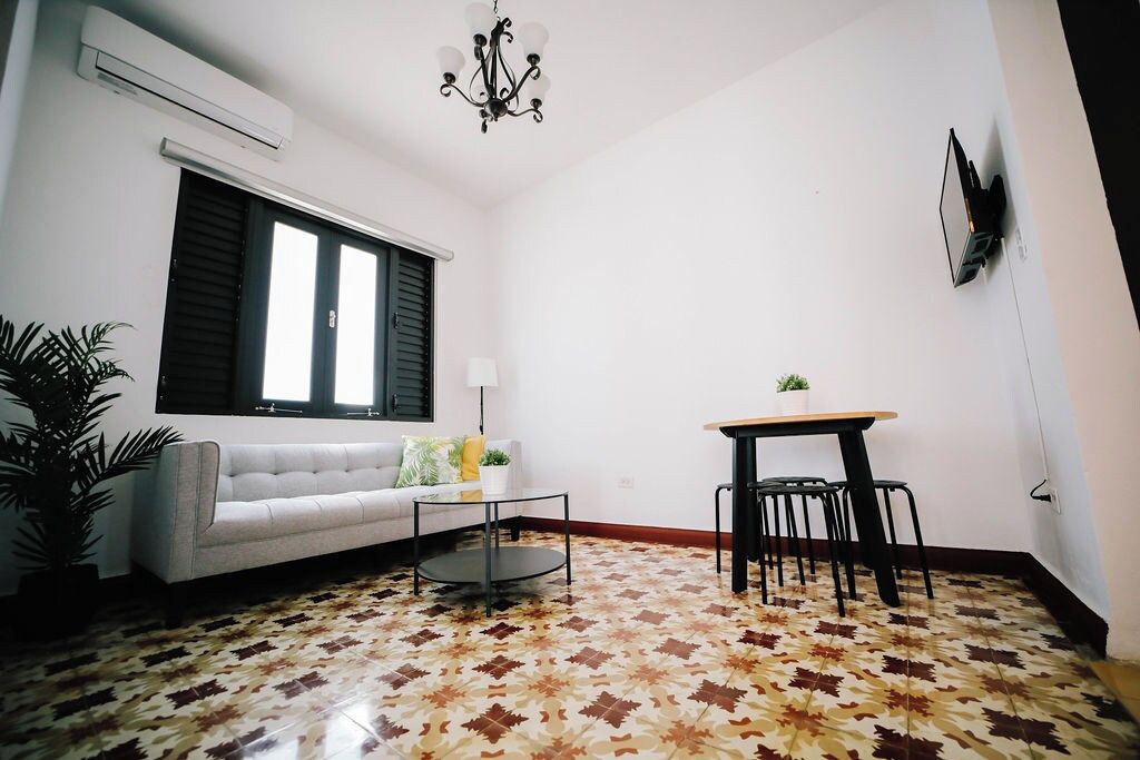 A living room with a sofa, a coffee table, a dining table with chairs, a potted plant, and a wall-mounted TV.