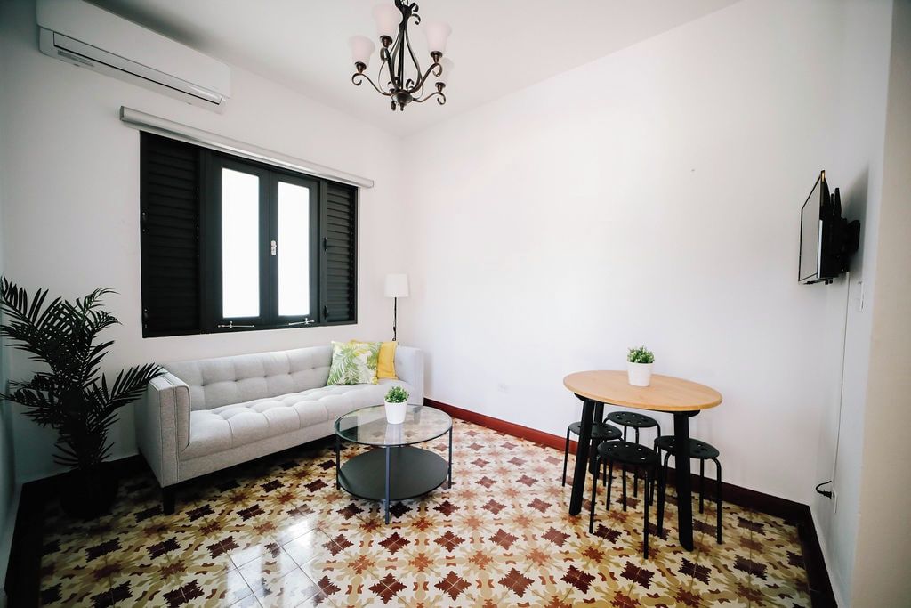 A living room with a sofa, a coffee table, a dining table with chairs, a potted plant, and a chandelier.