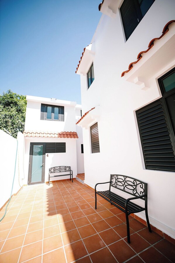 A white building with a tiled patio, a bench, and a door marked with the number 4.