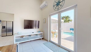 A modern room with a flat-screen TV, a built-in air conditioner, a sliding glass door leading to a pool area, and a white console table with books.