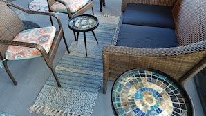 A patio area with wicker furniture, including a sofa and chairs, a small round table, and a mosaic floor. - Urban Ranch, at the Treasure House .. 8 bed 3 bath 2 kitchen + basement suite (Smyrna)