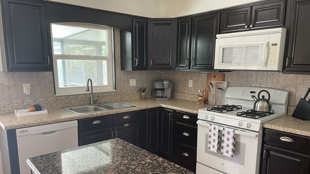 A kitchen with dark cabinets, a white stove, a microwave, and a window above the sink. - The Launch Pad - Perfect for viewing launches - minutes from beaches (Titusville)