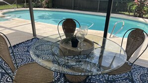 A glass-top table with wicker chairs and a patterned rug, near a swimming pool. - The Launch Pad - Perfect for viewing launches - minutes from beaches (Titusville)