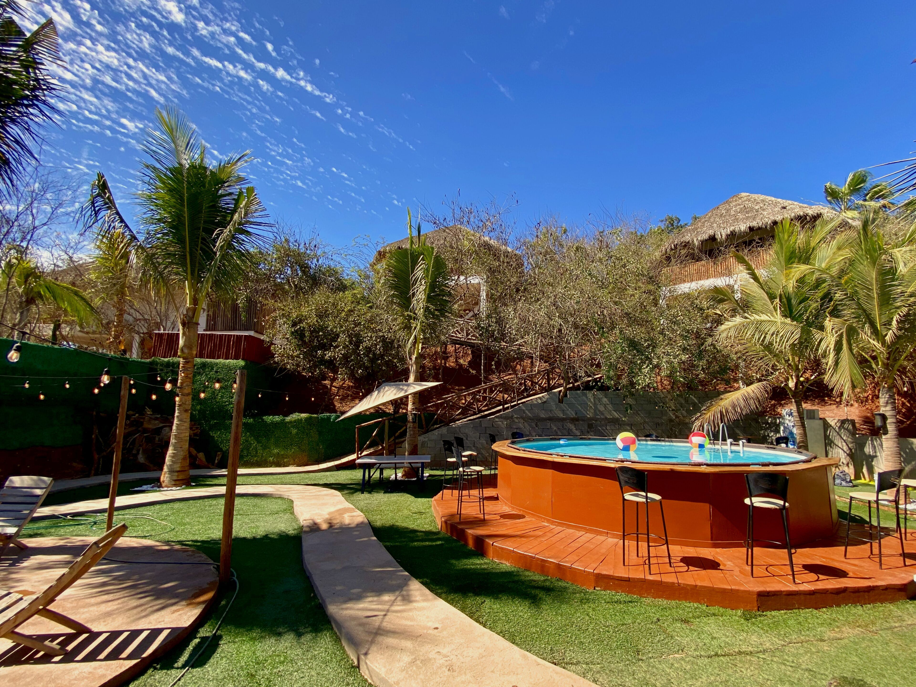 A pool area with a circular hot tub, lounge chairs, and a thatched-roof structure.