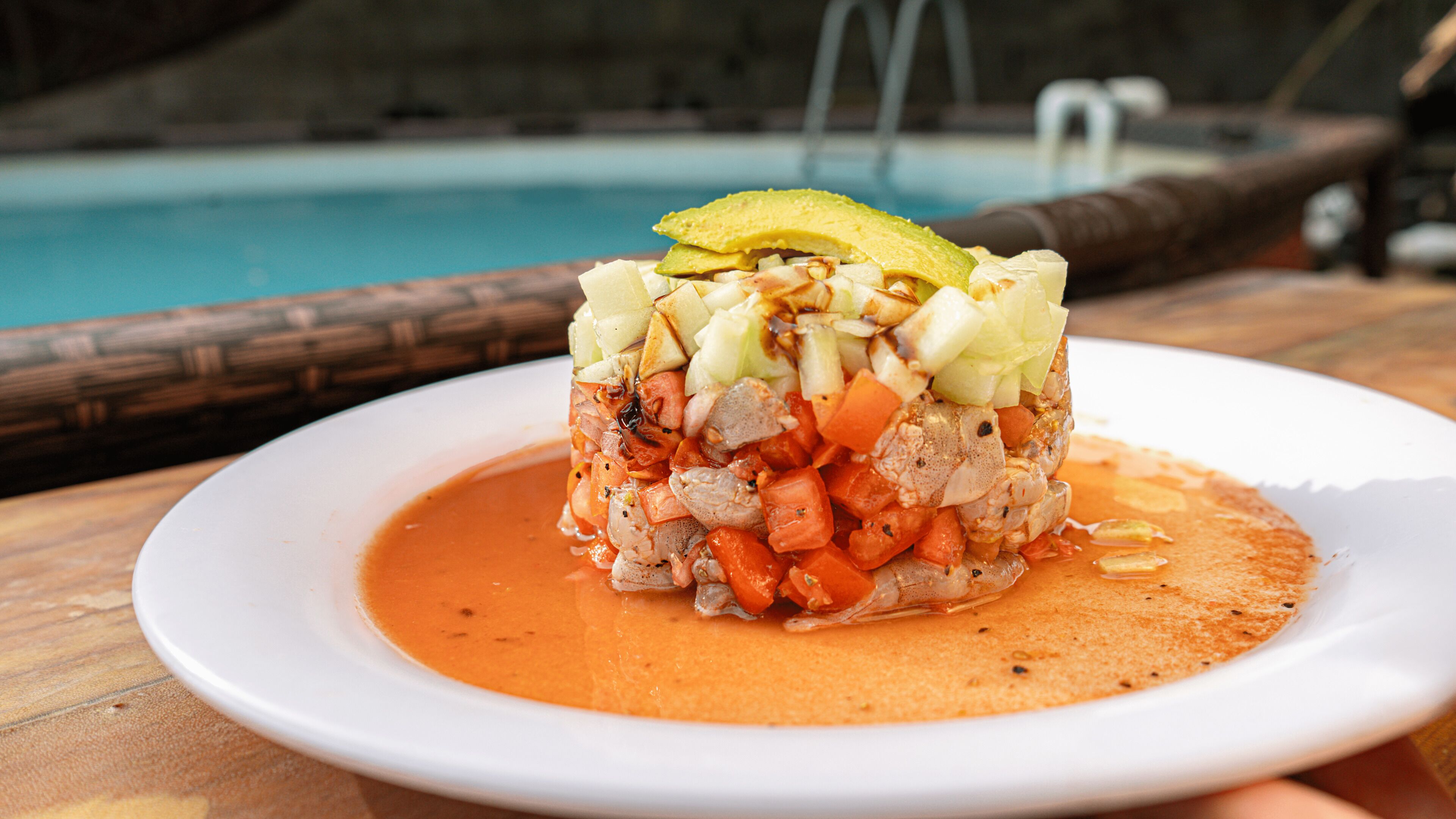 A dish with diced vegetables and meat, garnished with avocado, on a white plate.