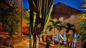 Un sendero conduce a un edificio con techo de paja, rodeado de cactus y palmeras.