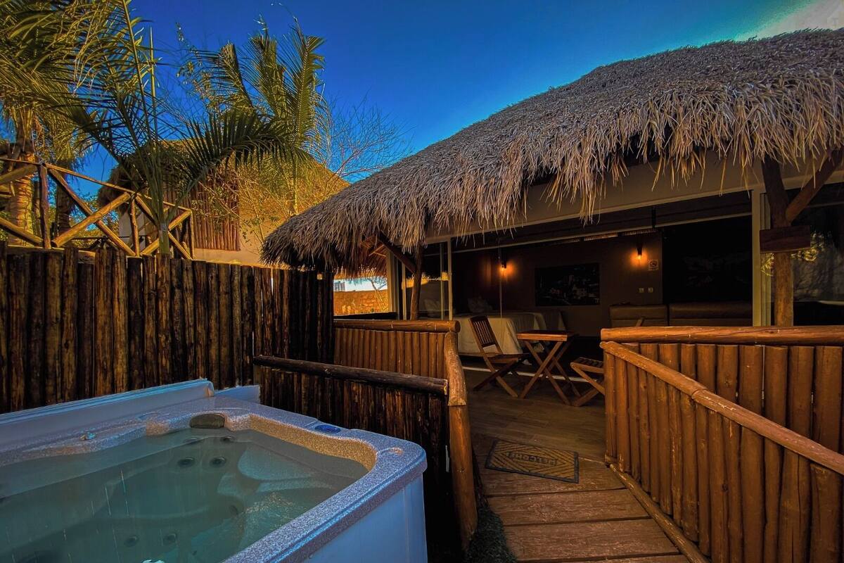 A wooden deck with a hot tub, a thatched-roof structure, and a view of palm trees.