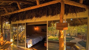 Una habitación con una cama, un banco de madera y un techo de paja.