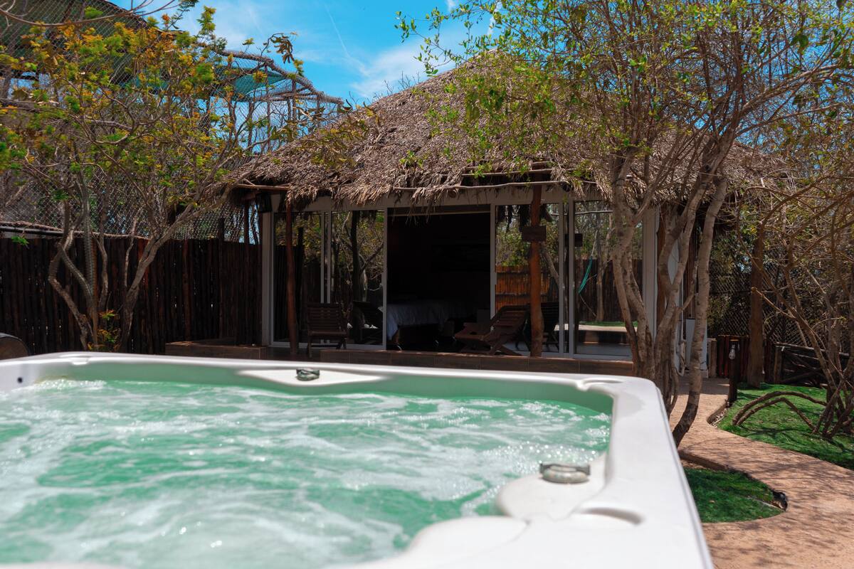 A hot tub in a backyard with a wooden deck, a covered seating area, and a fenced garden.