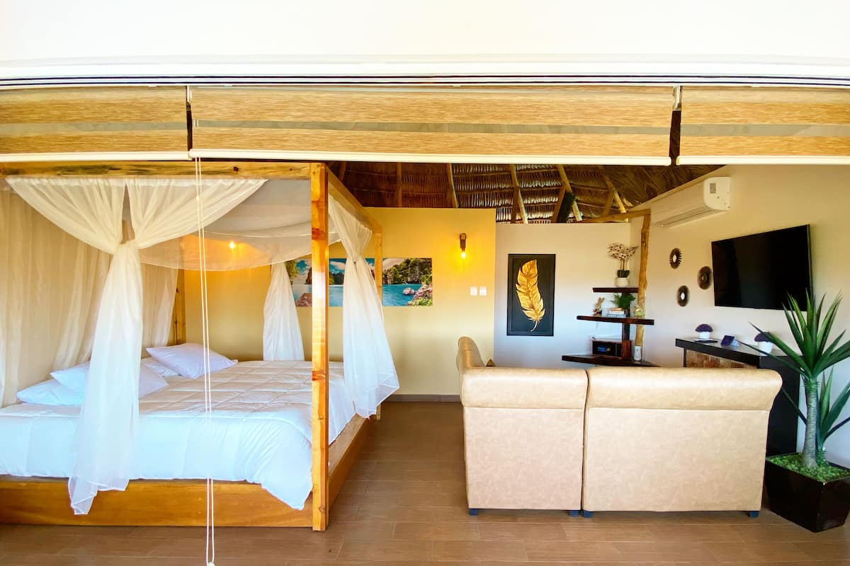 A bedroom with a canopy bed, a sofa, a TV, and a painting on the wall.