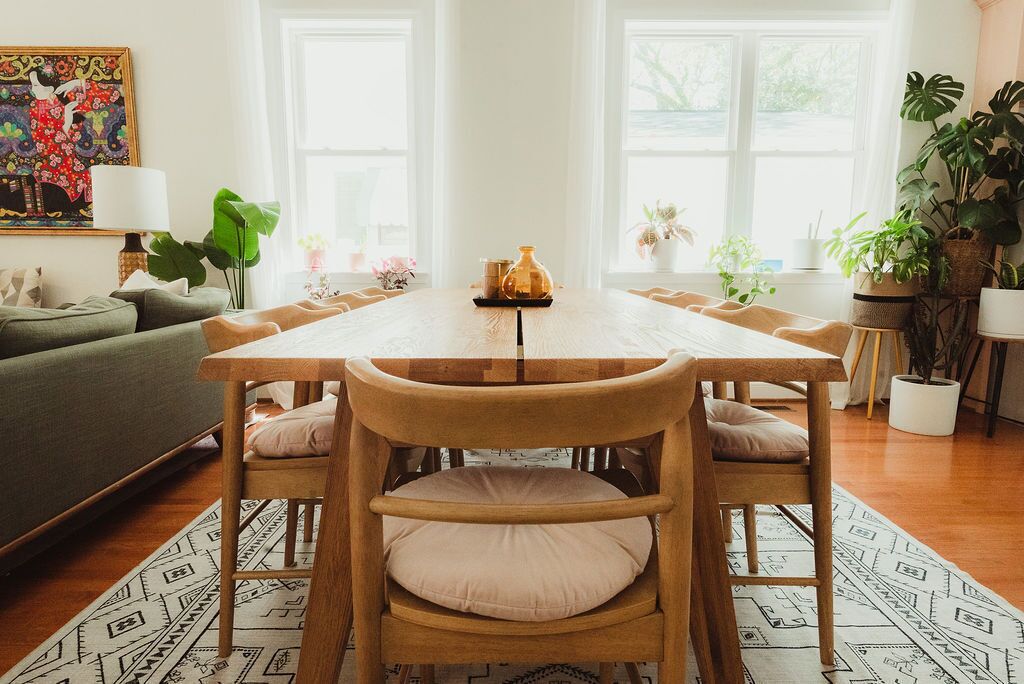 Een eetruimte met een houten tafel en stoelen, omringd door grote ramen en plantenbakken.