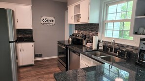 Une cuisine moderne avec des meubles blancs, un réfrigérateur en acier inoxydable, une cuisinière noire et une grande fenêtre.