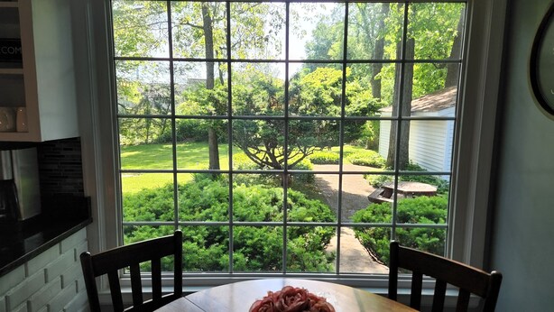 Un coin repas avec une table et des chaises, une fenêtre donnant sur un jardin et un mur en briques.