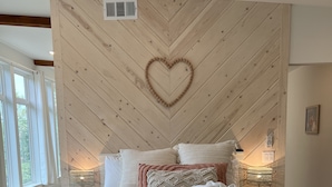 Un dormitorio con techo de madera en patrón de espiga, una decoración con forma de corazón y una cama con toallas enrolladas.