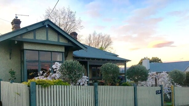 A two-story house with a green roof and a white picket fence. - Oozing character, romantic and cosy for two. (West Launceston)