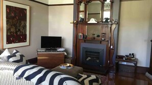 A living room with a fireplace, a television, and a framed painting on the wall. - Oozing character, romantic and cosy for two. (West Launceston)