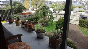 A covered porch with wooden furniture, potted plants, and a view of a residential area. - Oozing character, romantic and cosy for two. (West Launceston)