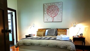 A neatly made bed with a patterned bedspread, two bedside lamps, and a wall-mounted artwork. - Oozing character, romantic and cosy for two. (West Launceston)