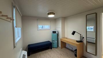 A small, well-lit room with a wooden desk, a bench, a microwave, and a large mirror.