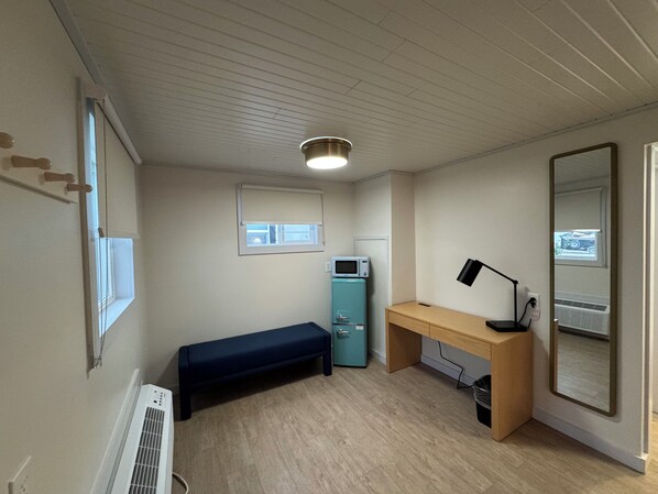 Une petite pièce bien éclairée, avec un bureau en bois, un banc, un four à micro-ondes et un grand miroir.