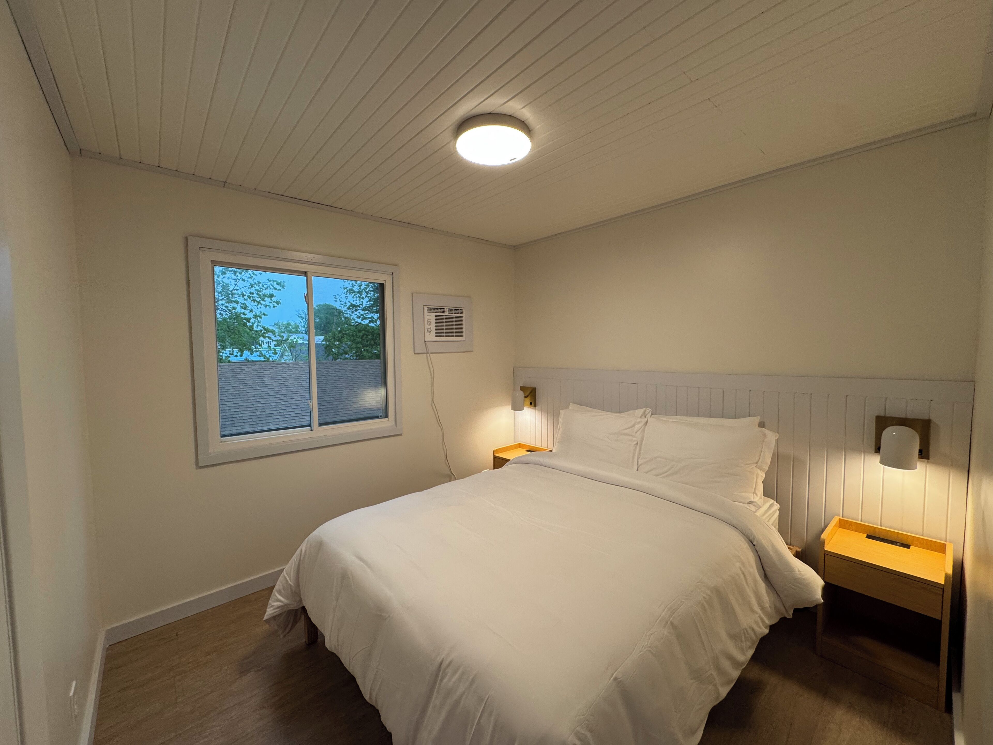 Un dormitorio con cama, ventana y un calefactor fijado a la pared.