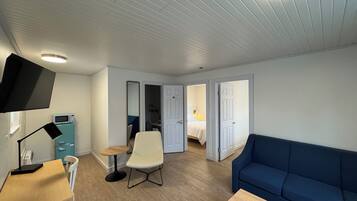 A room with a blue sofa, a wooden table, a white chair, a TV, and a microwave.