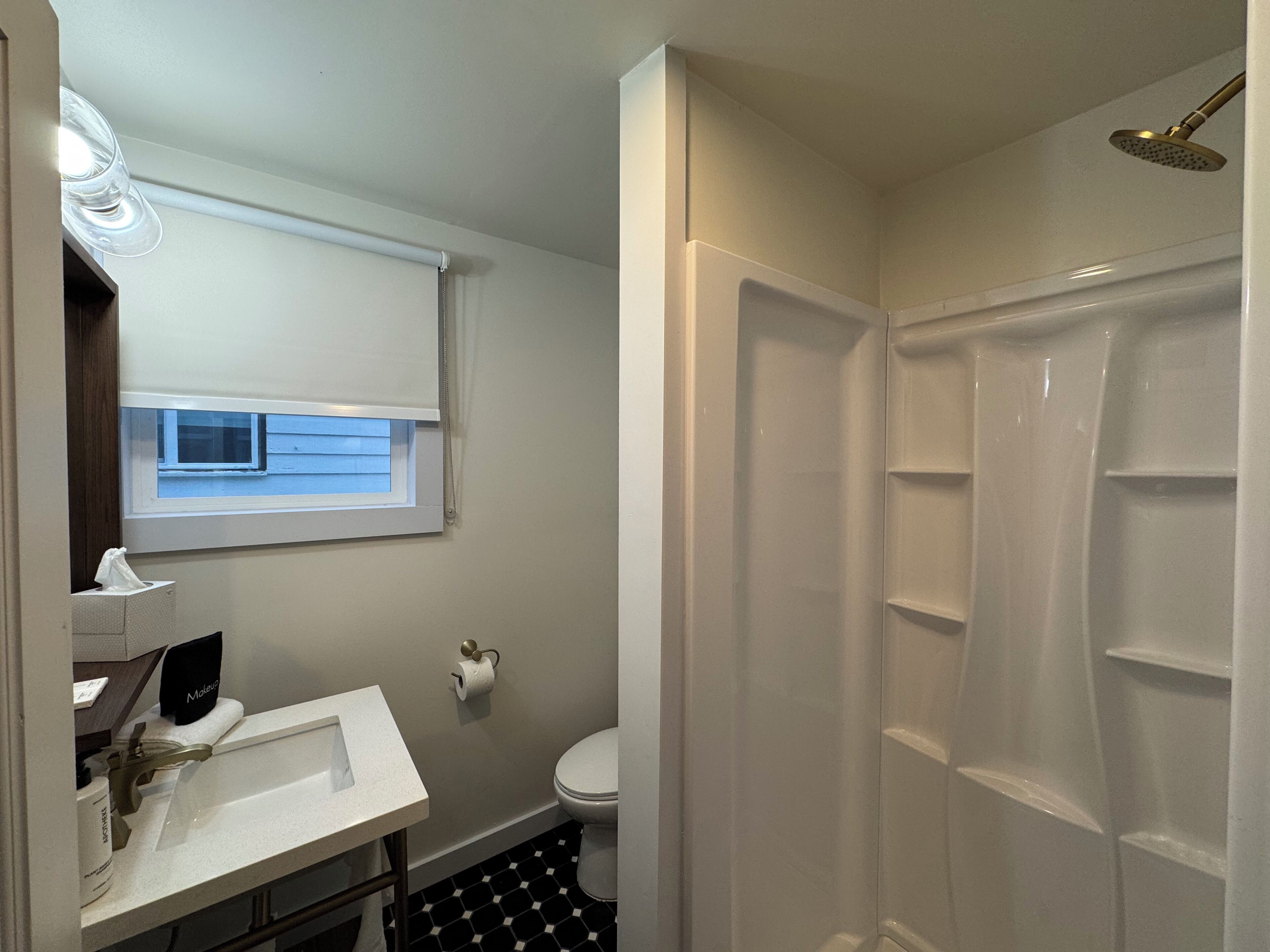 Un baño con lavamanos blanco, inodoro, ducha y ventana con persianas.