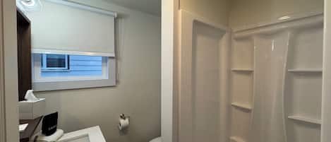 Un baño con lavamanos blanco, inodoro, ducha y ventana con persianas.