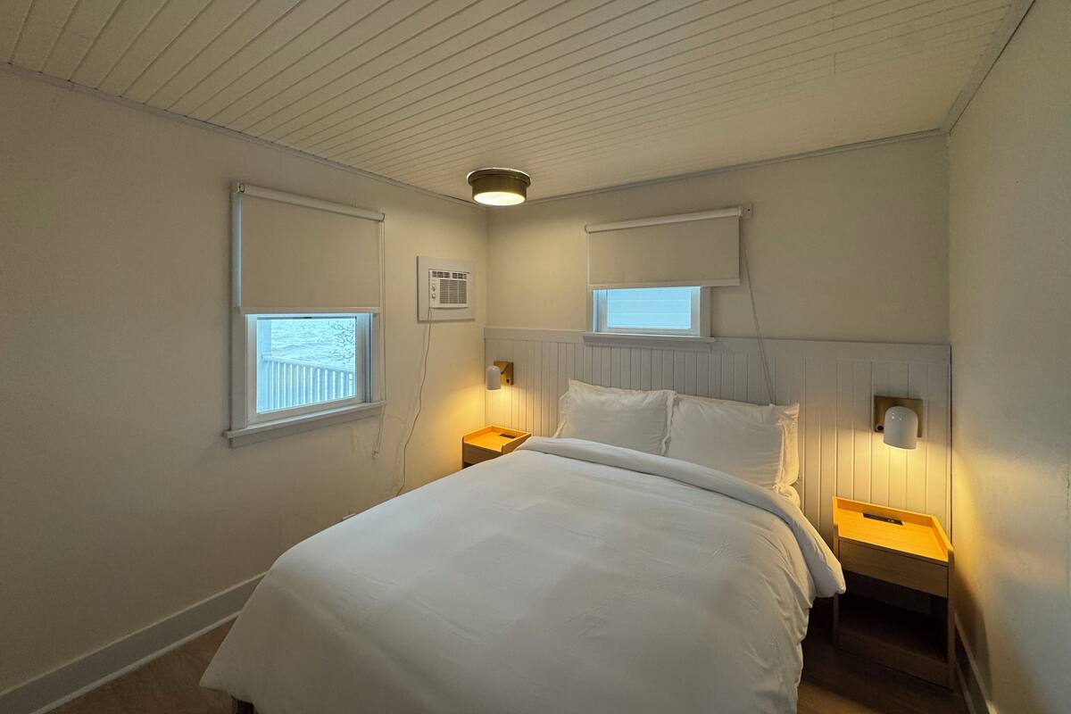 A bedroom with a bed, two bedside tables, a window, and a ceiling light.