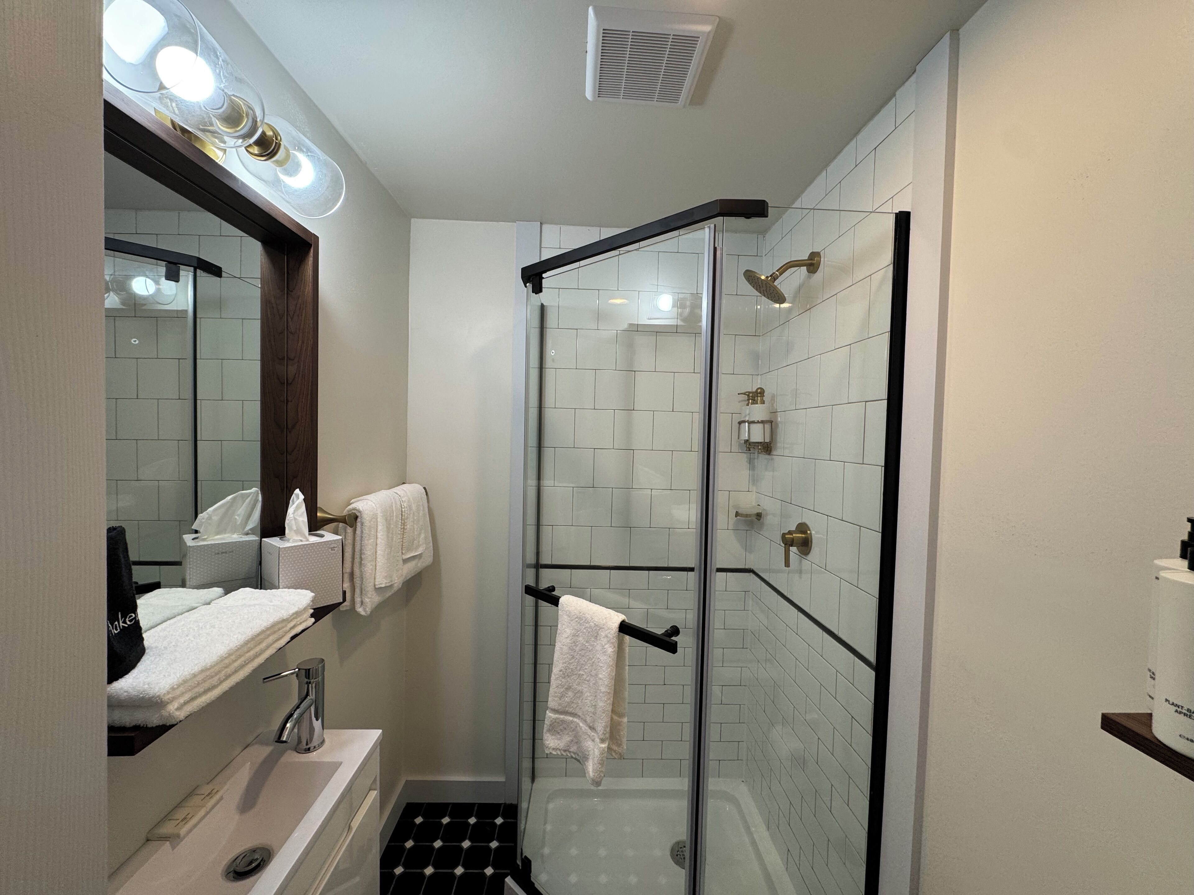 A modern bathroom with a glass-enclosed shower, white tiled walls, a vanity with a mirror, and a towel rack.