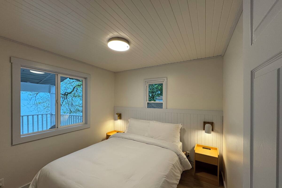 A bedroom with a single bed, two bedside tables, two wall-mounted lamps, and two windows.