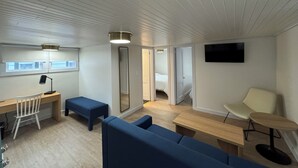 A modern room with a desk, chair, blue sofa, and a TV mounted on the wall. - The Ours at Geneva on the Lake (Geneva)
