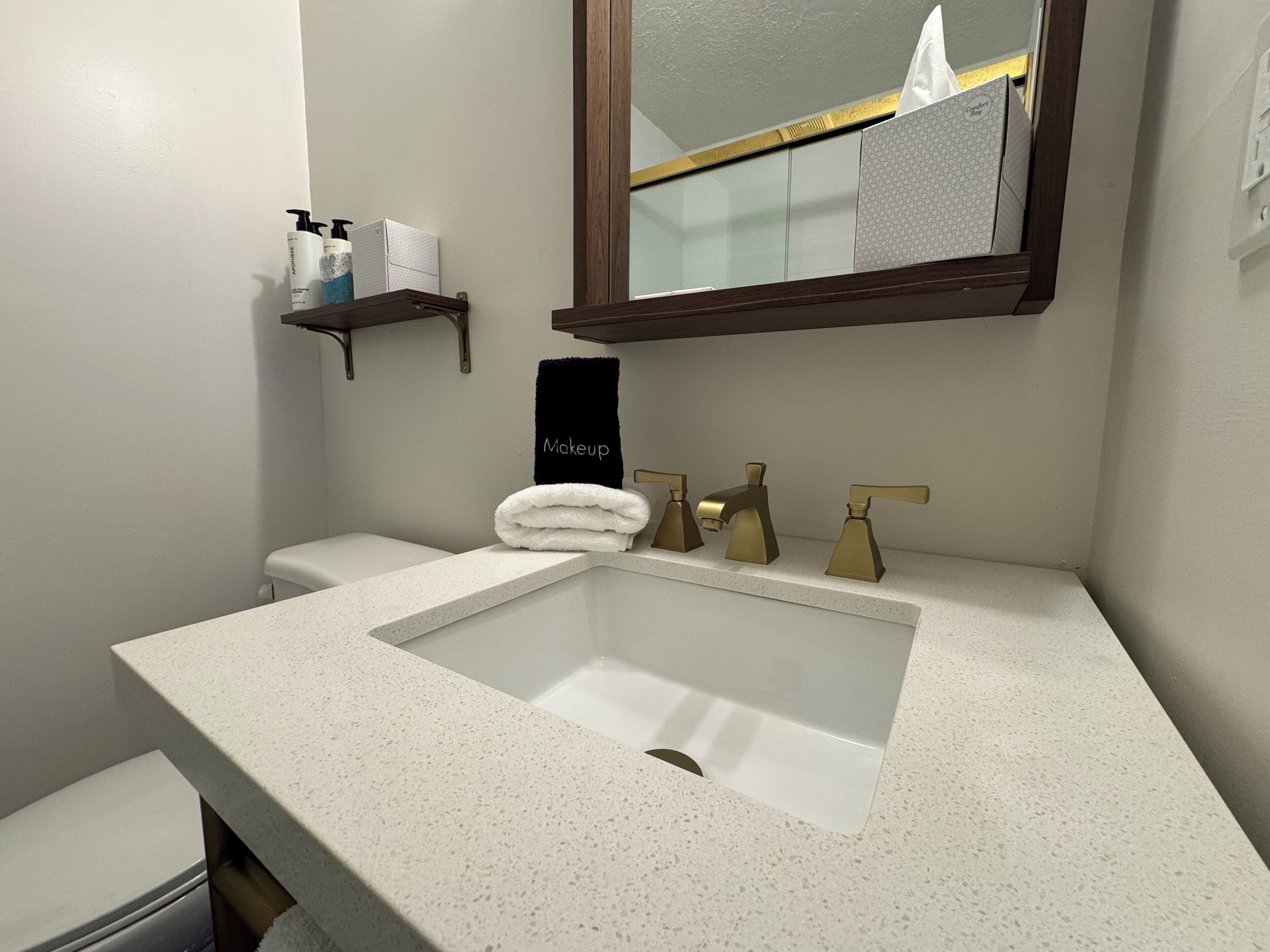 A bathroom with a white sink, a towel rack with a black towel labeled "Makeup," and a mirror above the sink.