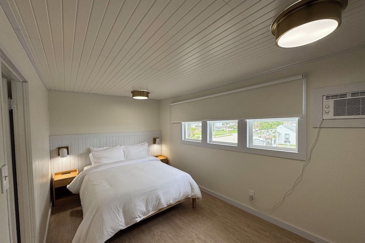 A bedroom with a bed, two bedside tables, a window with a view, and a ceiling light.