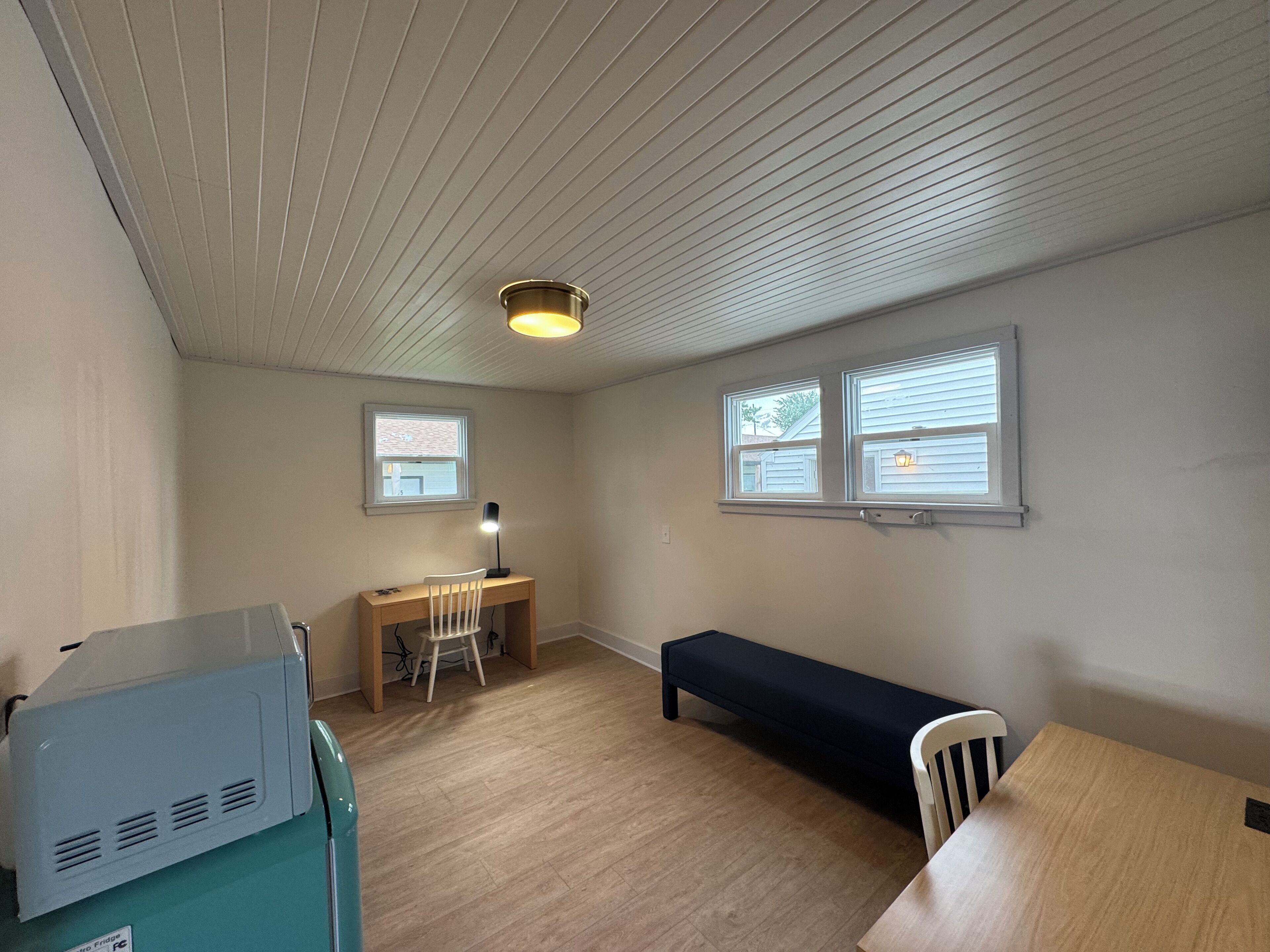 A room with a desk, chair, bench, and a ceiling fan.