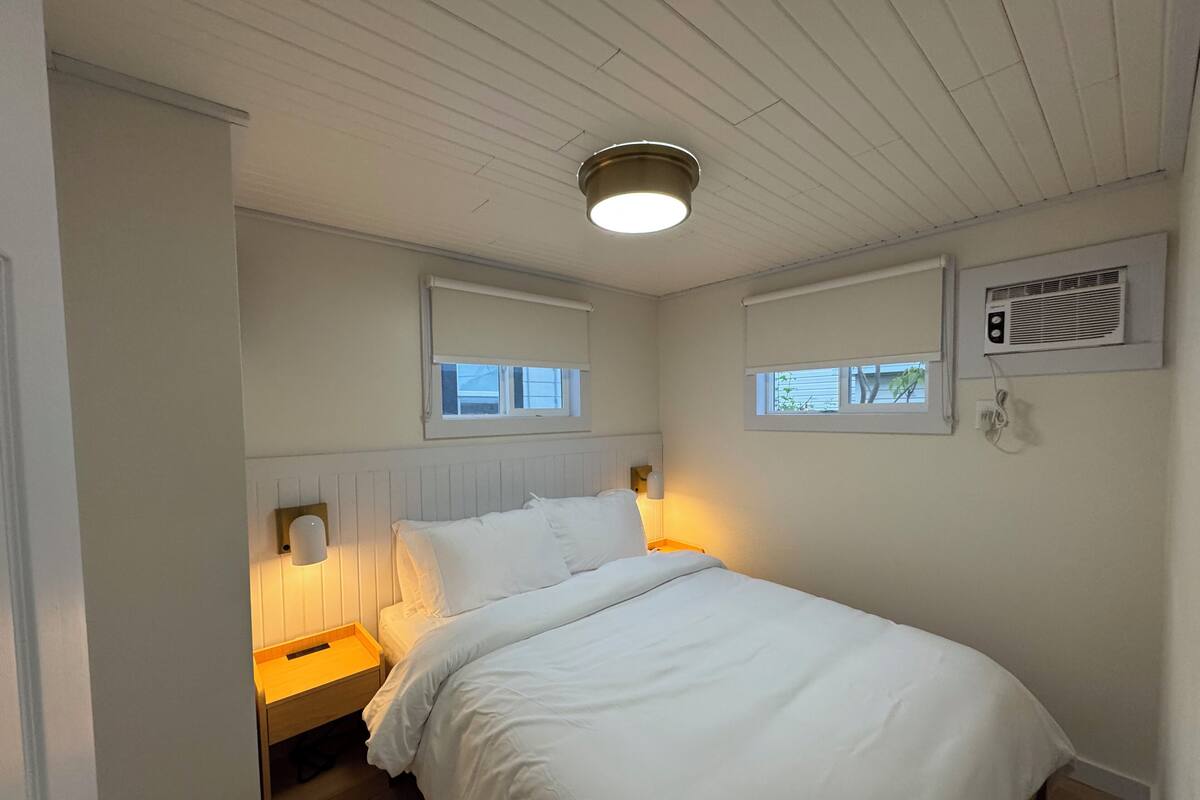 A bedroom with a bed, bedside tables, a window, and an air conditioning unit.
