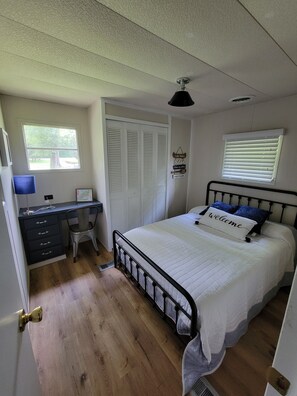 A bedroom with a bed, a desk, a chair, a window, and a door.