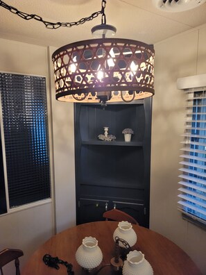 A dining area with a round table, a decorative hanging light fixture, and a black shelving unit with decorative items.