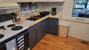 Une cuisine avec des meubles blancs, une cuisinière noire, une fenêtre donnant sur un paysage agréable et un panneau sur lequel on peut lire : « L’aventure vous attend ».
