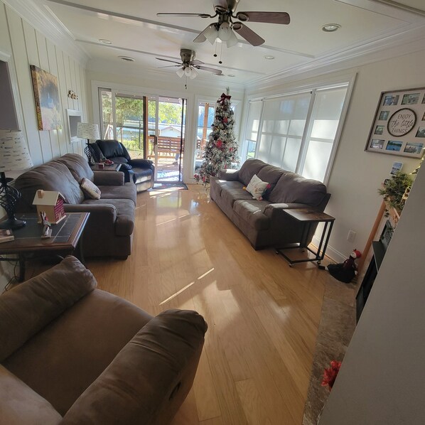 A spacious living room with a large window, a ceiling fan, and a Christmas tree.