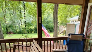 Une terrasse en bois avec une balançoire, une chaise bleue et une vue sur un jardin et une maison.