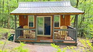 Een kleine hut met een veranda, twee stoelen en een deur.