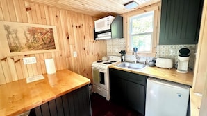 Een kleine keuken met houten wanden, een fornuis, een spoelbak en een koelkast.