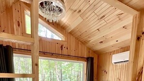 Een slaapkamer in een houten hut met een bed, een kroonluchter, een raam en een airconditioning.