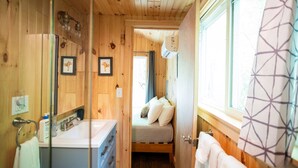 Een compact houten blokhut met een klein badkamertje, een bed en een raam.