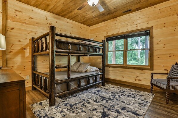 A bunk bed in a wooden cabin room with a window and a chair.