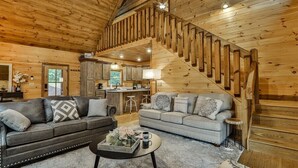 A wooden interior with a staircase, two sofas, a coffee table, and a kitchen area. - Happy Hideaway | Mineral Bluff, Ga (Mineral Bluff)